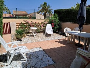 Un patio con sillones blancos, una mesa y un pequeño jardín con plantas y una palmera.