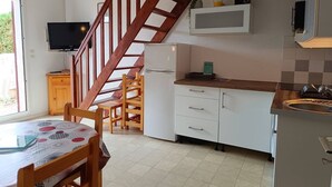 Eine Küche mit einer Holztreppe, einem Essbereich mit Tisch und Stühlen, einem Fernseher und einem Kühlschrank.