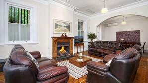 Een woonkamer met leren banken, een open haard en een eethoek met een tafelkleed met een patroon.