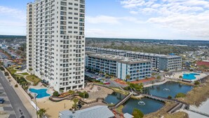 A high-rise hotel with multiple floors, a swimming pool, and a landscaped area with a small lake. - Unique Beachside Studio at Myrtle Beach Resort (Myrtle Beach)