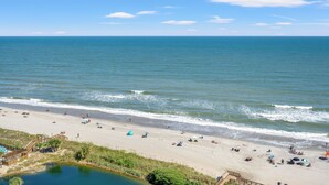 A beach with a wooden boardwalk leading to a small pond, a sandy beach with umbrellas, and the ocean in the background. - Unique Beachside Studio at Myrtle Beach Resort (Myrtle Beach)