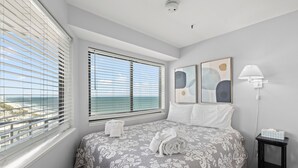 A bedroom with a bed, two windows with blinds, a bedside table with a lamp, and artwork on the wall. - Unique Beachside Studio at Myrtle Beach Resort (Myrtle Beach)