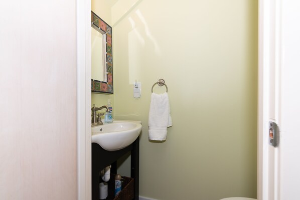 A bathroom with a white sink, a mirror with a colorful frame, a towel hanging on a ring, and a bottle of hand soap. - Ocean front villa taking in all views, walking distance to BHI Club; access to both clubs! (Bald Head Island)