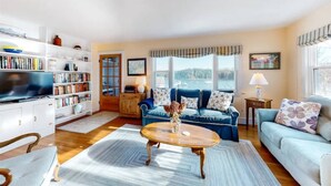A living room with a blue sofa, a coffee table, a bookshelf, and a television. -  "THE WAY LIFE SHOULD BE"
WATERFRONT OASIS /  HARBOR VIEWS AND A SHARED DOCK.
 (Cushing)
