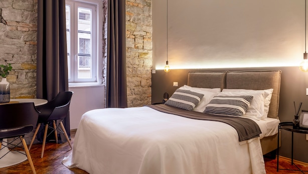 A modern bedroom with a stone wall, a bed with striped pillows, a desk with a chair, and a hanging light fixture. - Ghiberti  - Romantic Studio in Trieste (Trieste)