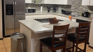 A modern kitchen with a central island, stainless steel appliances, and a ceiling fan.