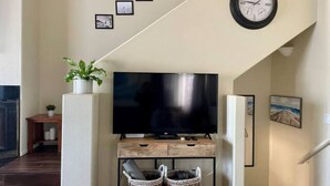 Ein Wohnzimmer mit einem Flachbildfernseher auf einem Holzständer, einer Uhr an der Wand und einer Treppe, die zu einer anderen Ebene führt.