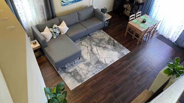Ein Wohnzimmer mit grauem Sofa, einem Couchtisch und einem Essbereich mit Tisch und Stühlen.