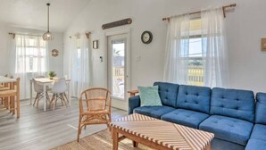 A living room with a blue sofa, a wooden coffee table, and a dining area with a table and chairs. - Sun-Filled 3 Bedroom House - Steps from the Beach (Surfside Beach)