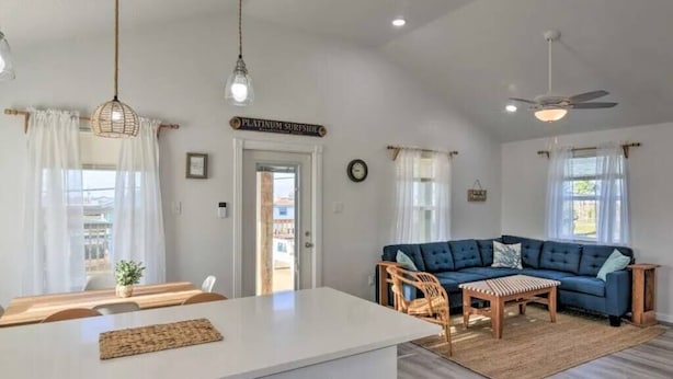 A spacious living area with a blue sofa, a wooden coffee table, and a white island. There is a ceiling fan and a sign above the door. - Sun-Filled 3 Bedroom House - Steps from the Beach (Surfside Beach)