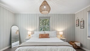 Une chambre à coucher avec un grand lit, deux lampes de chevet, un luminaire suspendu, un miroir et une fenêtre avec des stores.