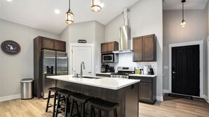 A modern kitchen with a central island, stainless steel appliances, and bar stools. - Tranquil Jewel: Arcade, King Suits, Hot Tub, Decks (Sand Lake)