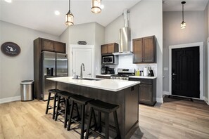 A modern kitchen with a central island, stainless steel appliances, and bar stools. - Tranquil Jewel: Arcade, King Suits, Hot Tub, Decks (Sand Lake)
