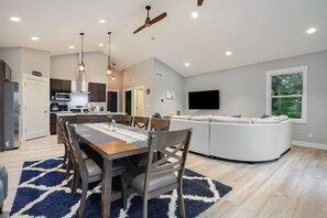 A modern kitchen with a dining area, a large window, and a ceiling fan.