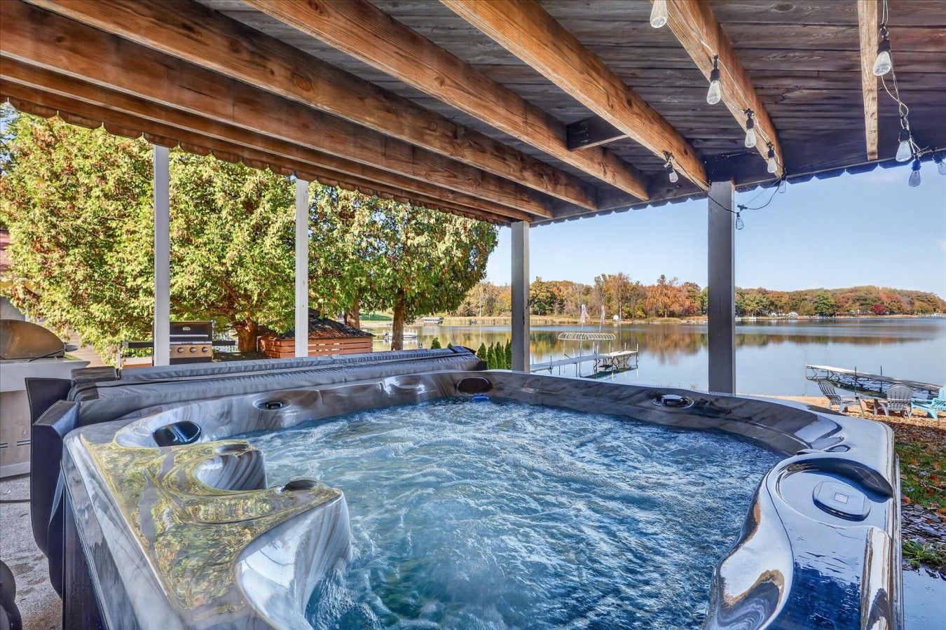 Een hottub met een houten pergola erboven, omgeven door bomen en uitzicht op een meer.