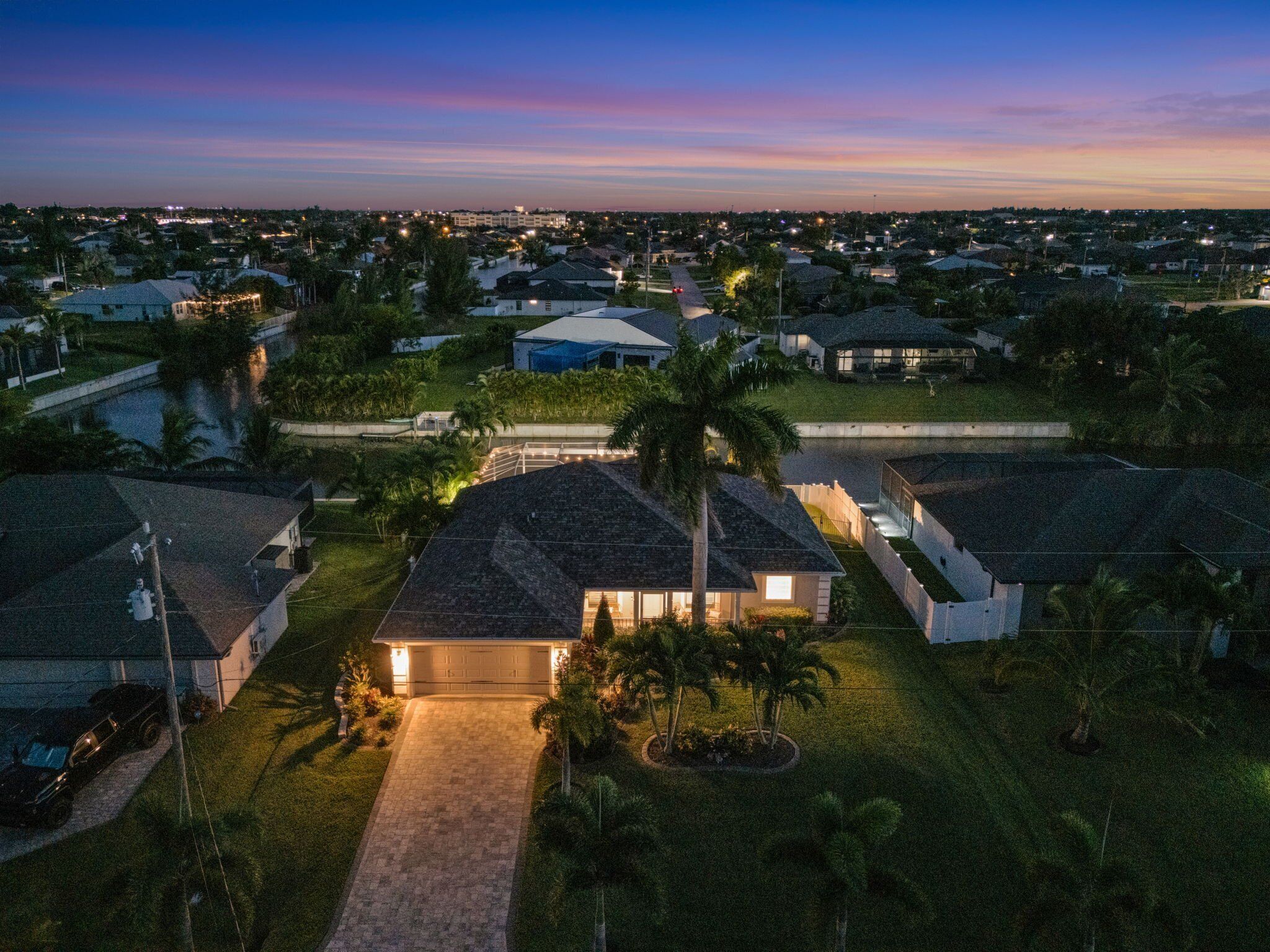 Un quartier résidentiel au crépuscule, avec des maisons, une allée pavée et un palmier.