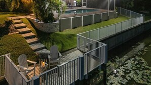 Un espace extérieur bien éclairé, doté d’une piscine, d’un coin salon abrité et d’une terrasse en bois avec des chaises.
