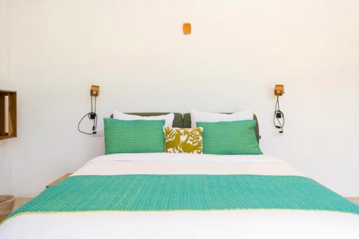 Una cama con ropa de cama verde y blanca, dos almohadas verdes y dos lámparas fijadas a la pared.