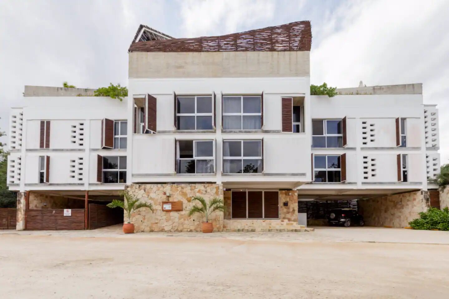 Un edificio moderno de varios pisos con techo plano, ventanas amplias y un patio central con plantas en macetas.