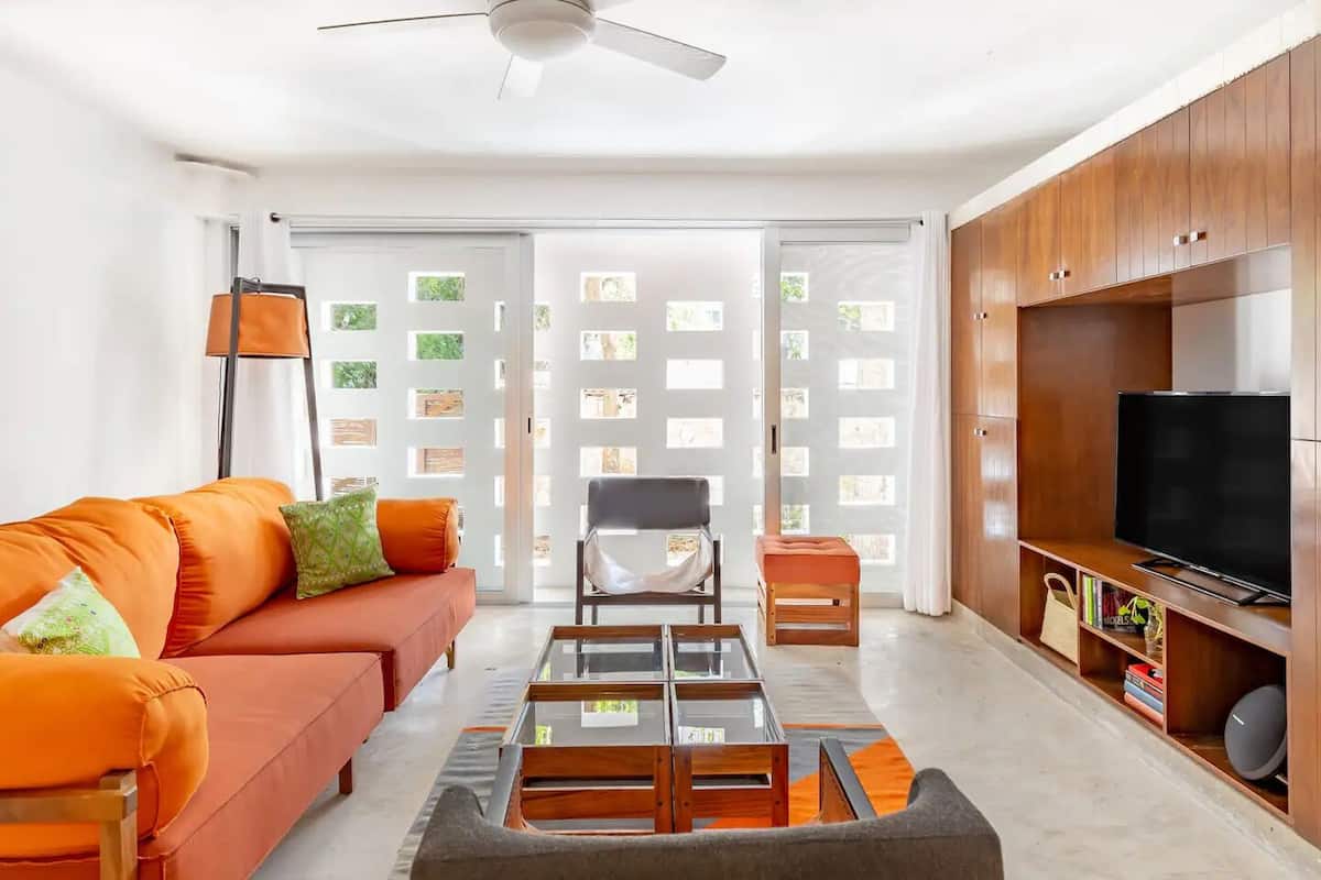 Una sala de estar moderna con sofá, sillón, reposapiés, mesa de centro, televisor y armarios de madera.