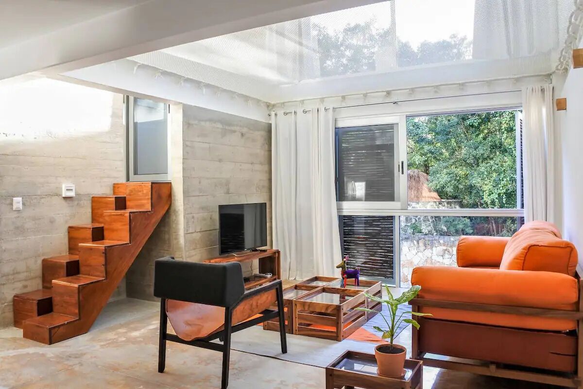 Un salon moderne avec un escalier en bois, un canapé, une table basse et un téléviseur.
