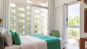 Una camera da letto con un letto, un cuscino verde, un cuscino bianco, una coperta verde e un comodino in legno, oltre a una finestra che si affaccia sul verde.