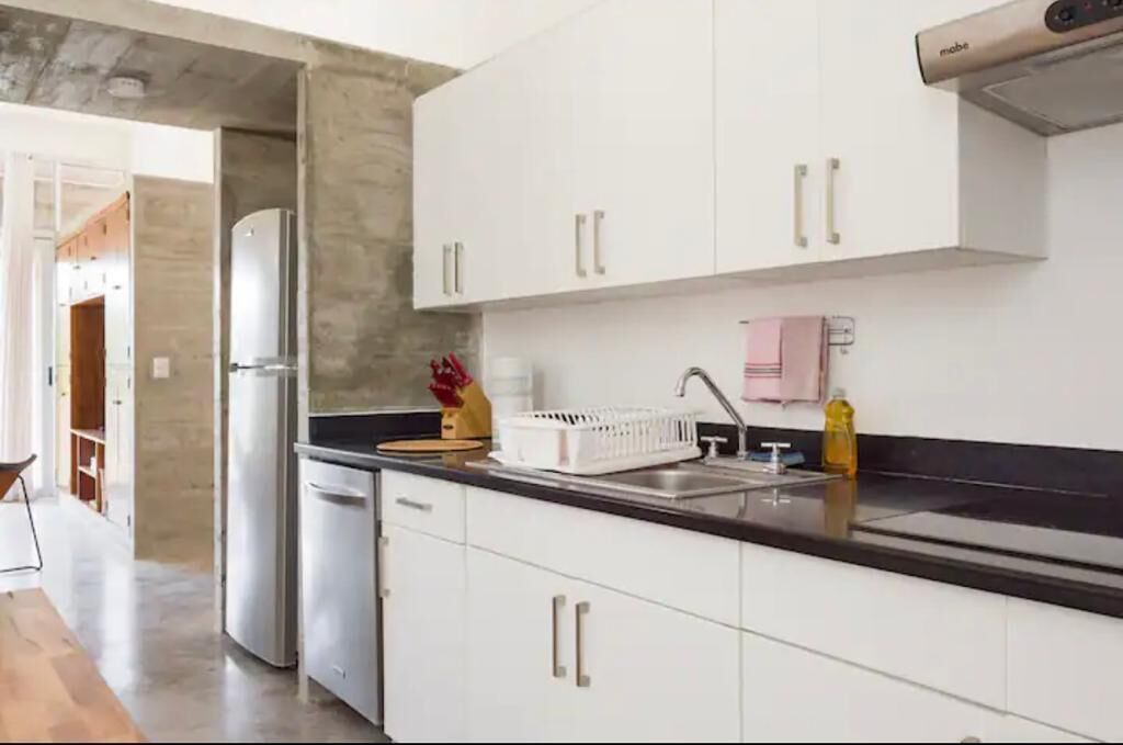 A modern kitchen with white cabinets, a stainless steel refrigerator, and a black countertop.
