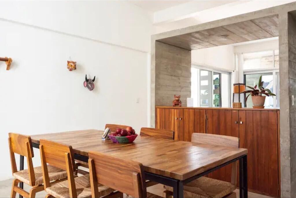 A dining area with a wooden table and chairs, a fruit bowl, and a wooden cabinet with a cat figurine.