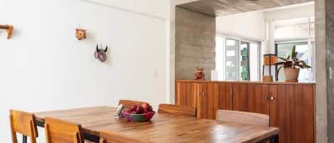 A dining area with a wooden table and chairs, a fruit bowl, and a wooden cabinet with a cat figurine.