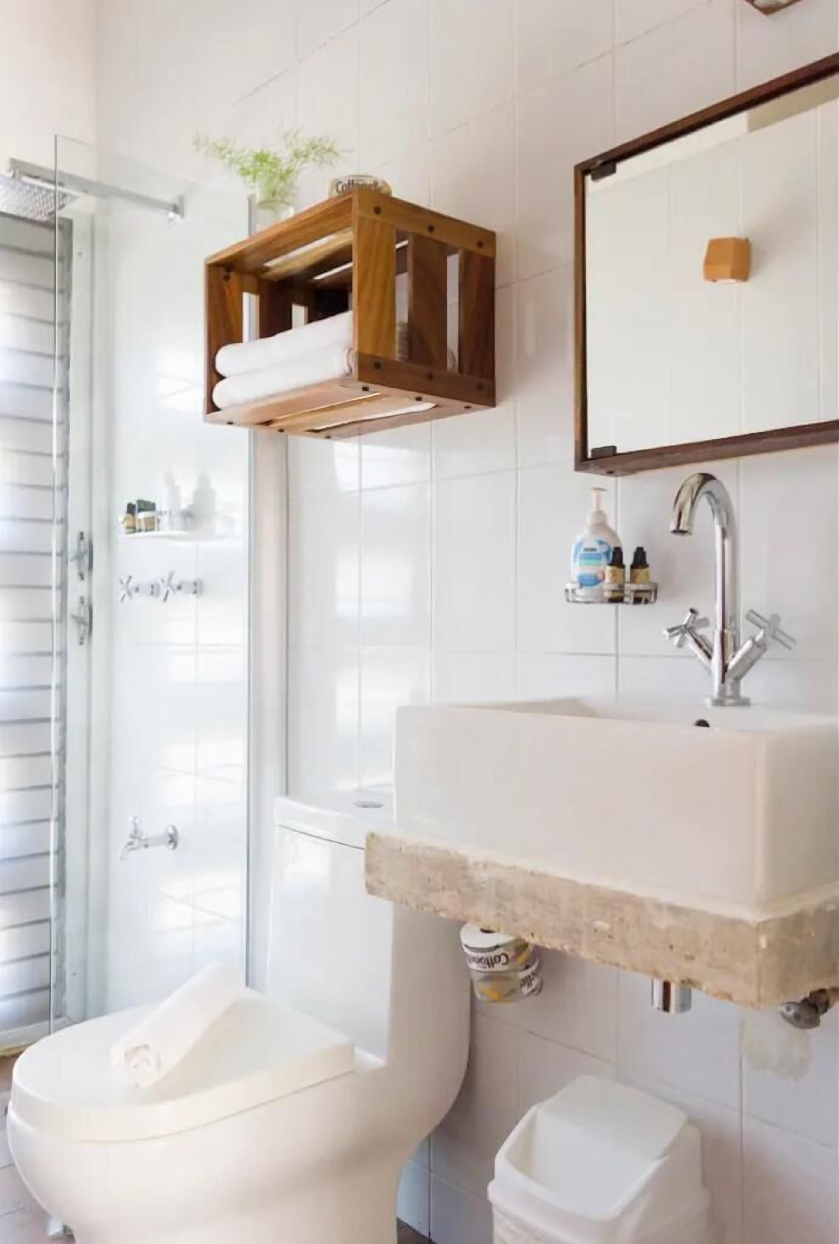A bathroom with a white toilet, a sink with a wooden shelf above it, and a mirror.