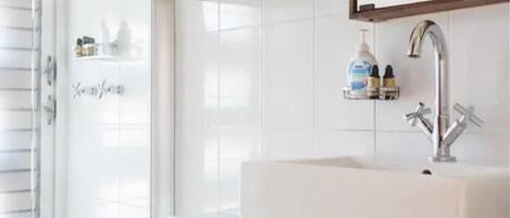 A bathroom with a white toilet, a sink with a wooden shelf above it, and a mirror.