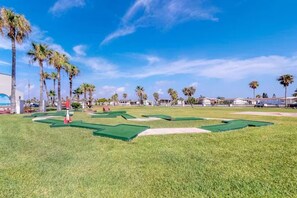 Ein Golfplatz mit grünen Spielbahnen, Sandbunkern und Palmen.