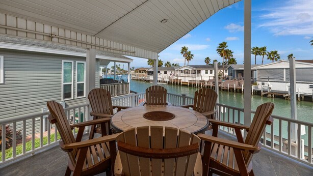 A covered outdoor seating area with a round table and chairs, overlooking a marina with docked boats and houses. - Long Island Village Texas (Port Isabel)
