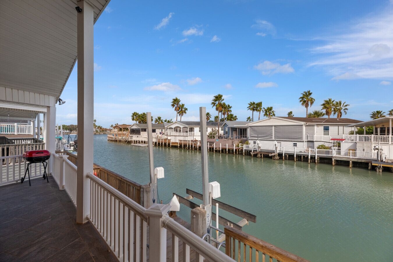 A waterfront property with a covered deck, a grill, and multiple docked boats.
