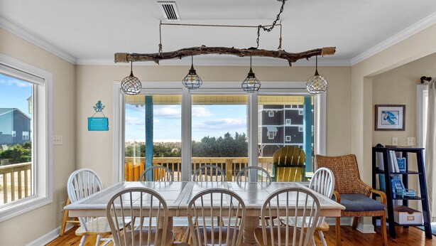 A dining area with a long table and six chairs, a wooden ceiling, and a view through large windows. - 5 BR Oceanview home with hot tub and pet friendly! (Oak Island)
