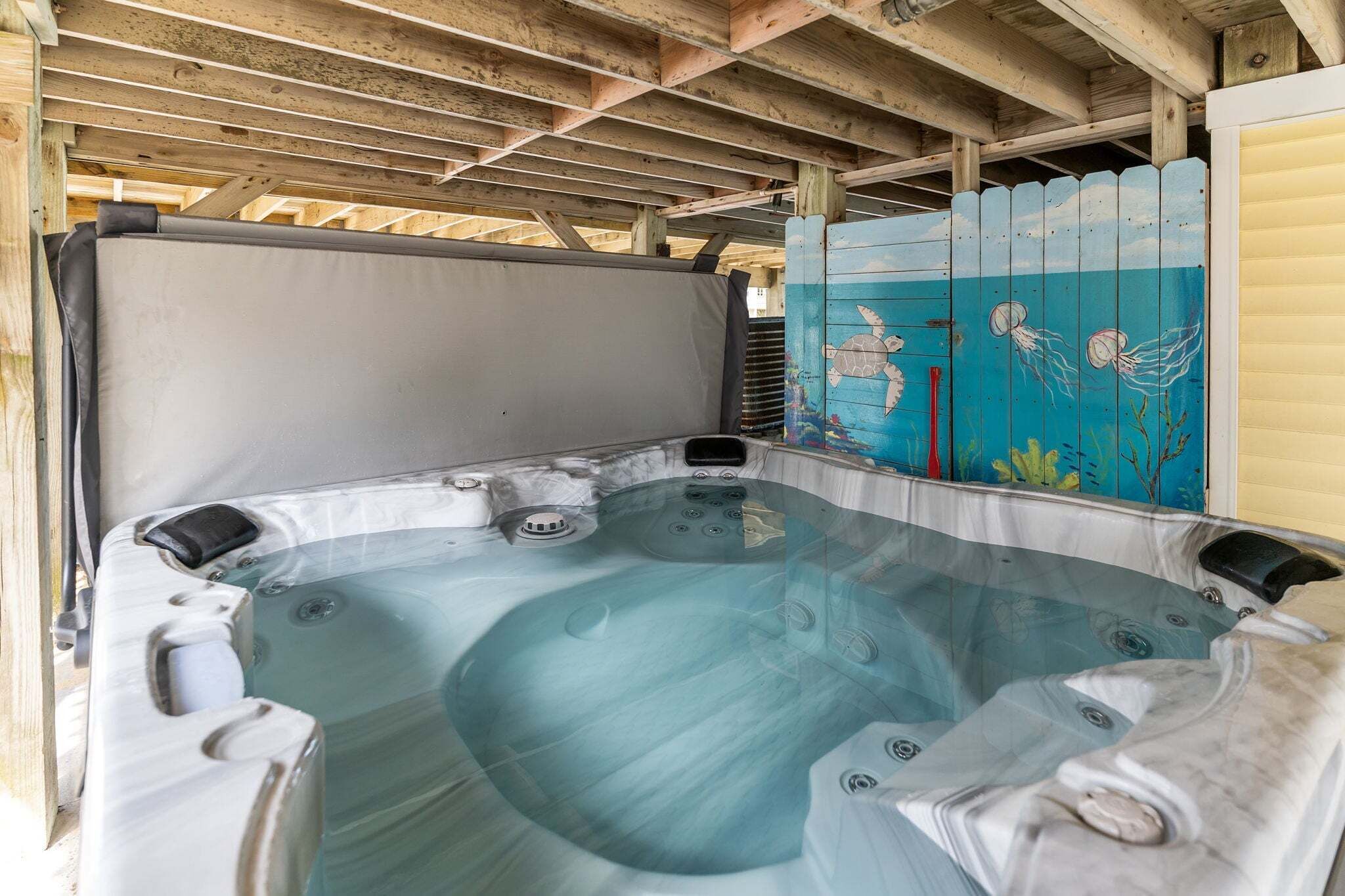 A hot tub with a glass enclosure, wooden beams, and a painted fence with marine life.