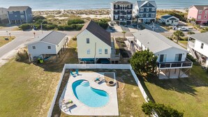 A residential area with a swimming pool, houses, and a beach in the background. - 5 BR Oceanview home with hot tub and pet friendly! (Oak Island)