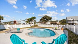 A swimming pool with a curved edge, surrounded by a white fence, and two turquoise chairs in the foreground. - 5 BR Oceanview home with hot tub and pet friendly! (Oak Island)