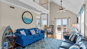 A spacious living room with a blue sofa, a patterned rug, and a view of the outdoors. - 5 BR Oceanview home with hot tub and pet friendly! (Oak Island)