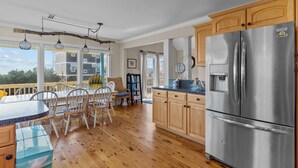 A kitchen with wooden cabinets, a stainless steel refrigerator, and a dining area with chairs and a table. - 5 BR Oceanview home with hot tub and pet friendly! (Oak Island)