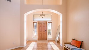 Un hall d’entrée spacieux avec une porte en bois, un banc doté de coussins et un luminaire au plafond.