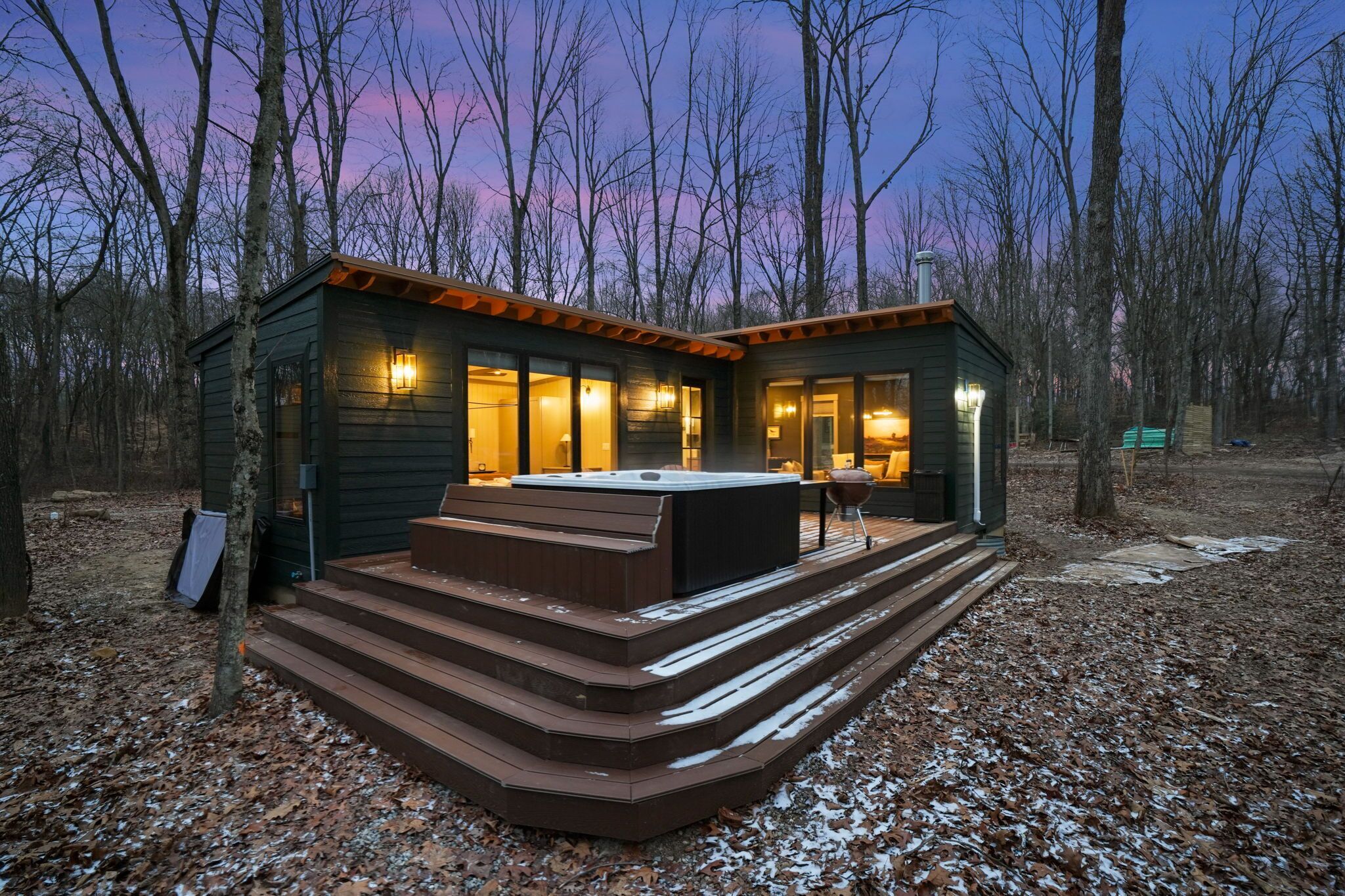 Una cabaña con jacuzzi, terraza de madera y vistas al bosque circundante.