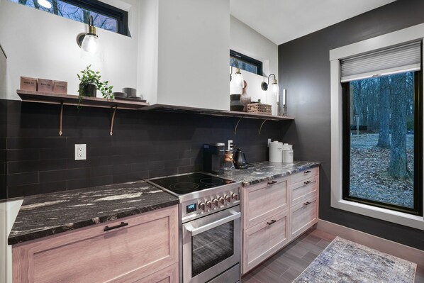 A modern kitchen with a black countertop, stainless steel appliances, and a window with a view of trees.