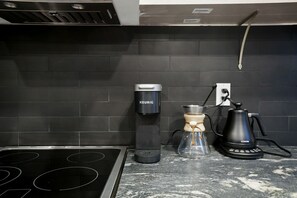 A kitchen with a black tiled backsplash, a Keurig coffee maker, a glass carafe, and a Cosori coffee pot.