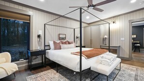 Een moderne slaapkamer met een hemelbed, uitzicht op het bos door een raam en een plafondventilator.