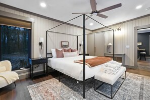Une chambre à coucher moderne avec un lit à baldaquin, une vue sur la forêt par la fenêtre et un ventilateur de plafond.