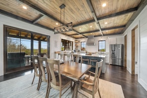 A spacious kitchen with a large island, wooden ceiling beams, and a stainless steel refrigerator.