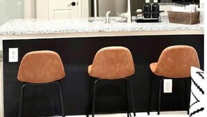 Une cuisine moderne avec des meubles blancs, un réfrigérateur en acier inoxydable, un plan de travail en marbre et trois tabourets de bar.