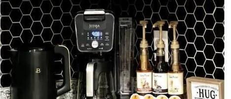 A kitchen counter with a coffee maker, a mug, and a coffee station with pumps and containers.