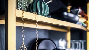 A kitchen shelf with cookware, a hanging geometric decoration, and a green bowl.